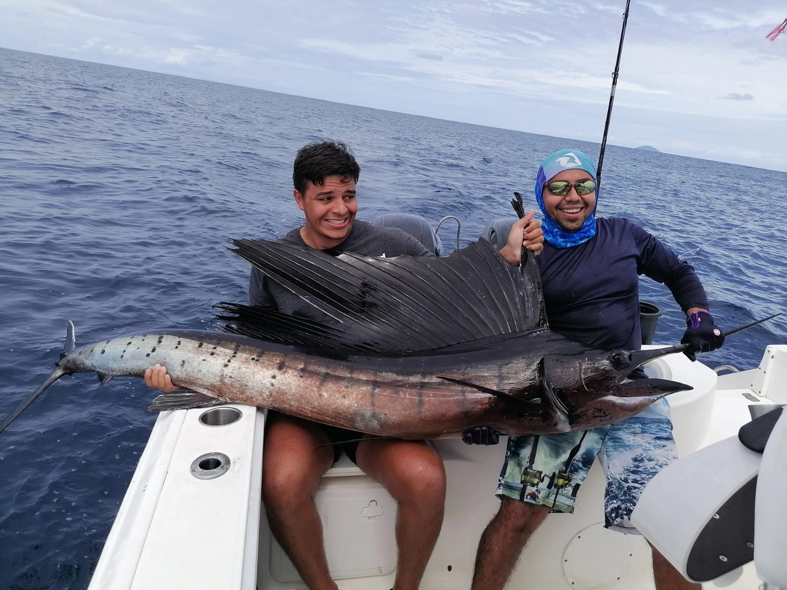 Captura y liberación de Pez Vela - En las cristalinas aguas de Coiba, un pescador sostiene con orgullo un pez vela recién capturado. La majestuosidad del pez brilla bajo el sol antes de ser liberado nuevamente en su hábitat natural, en un acto de respeto y admiración por la vida marina.